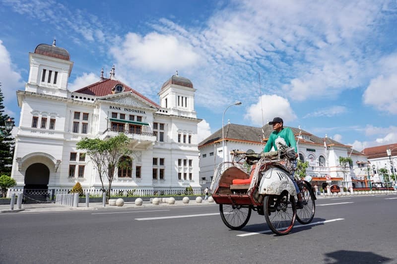 A becak rider passing the white colonial Bank Indonesia building in Yogyakarta