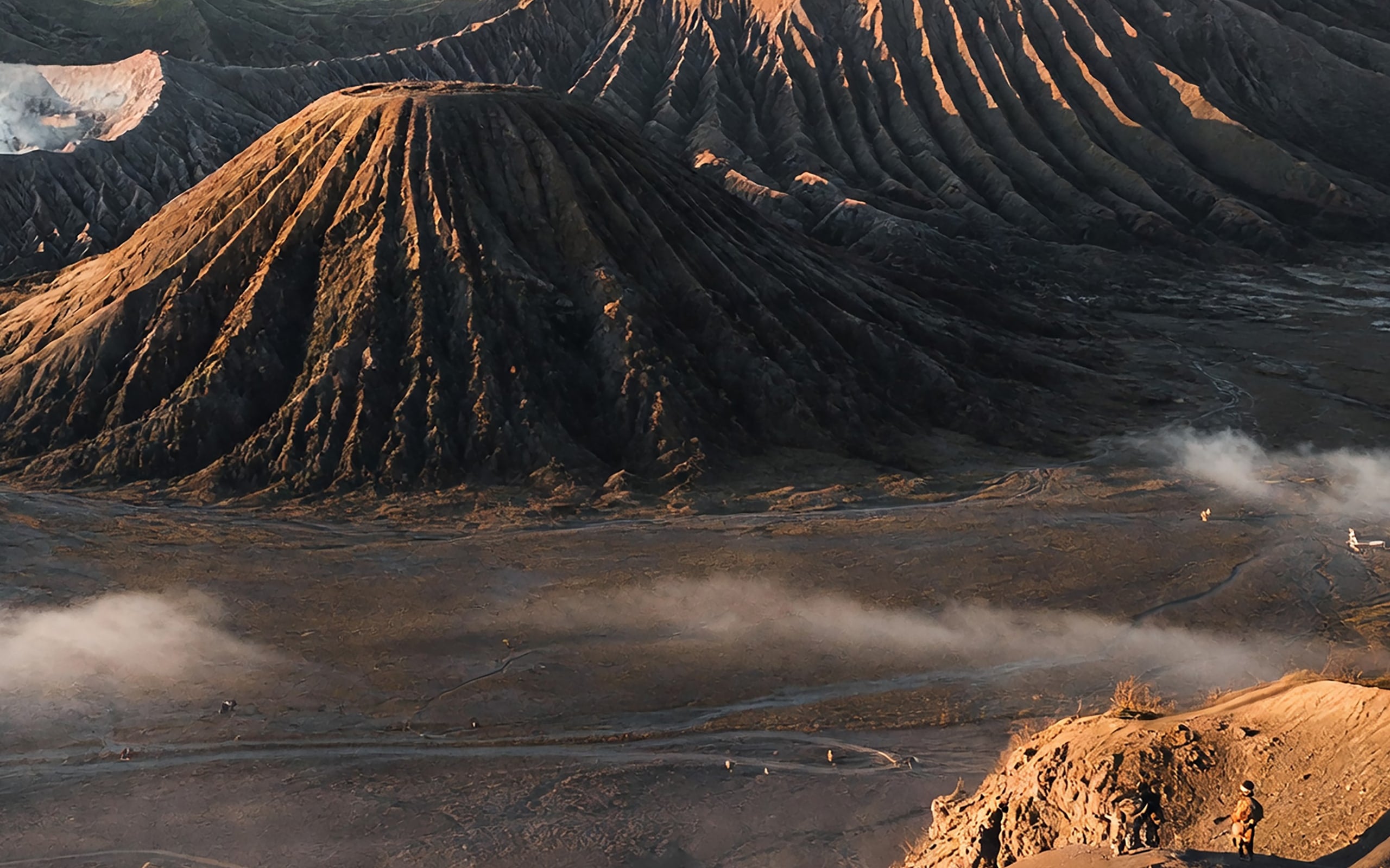 The cones of Mount Batok and Mount Bromo in low sunrise light, with riders crossing the sand sea far below